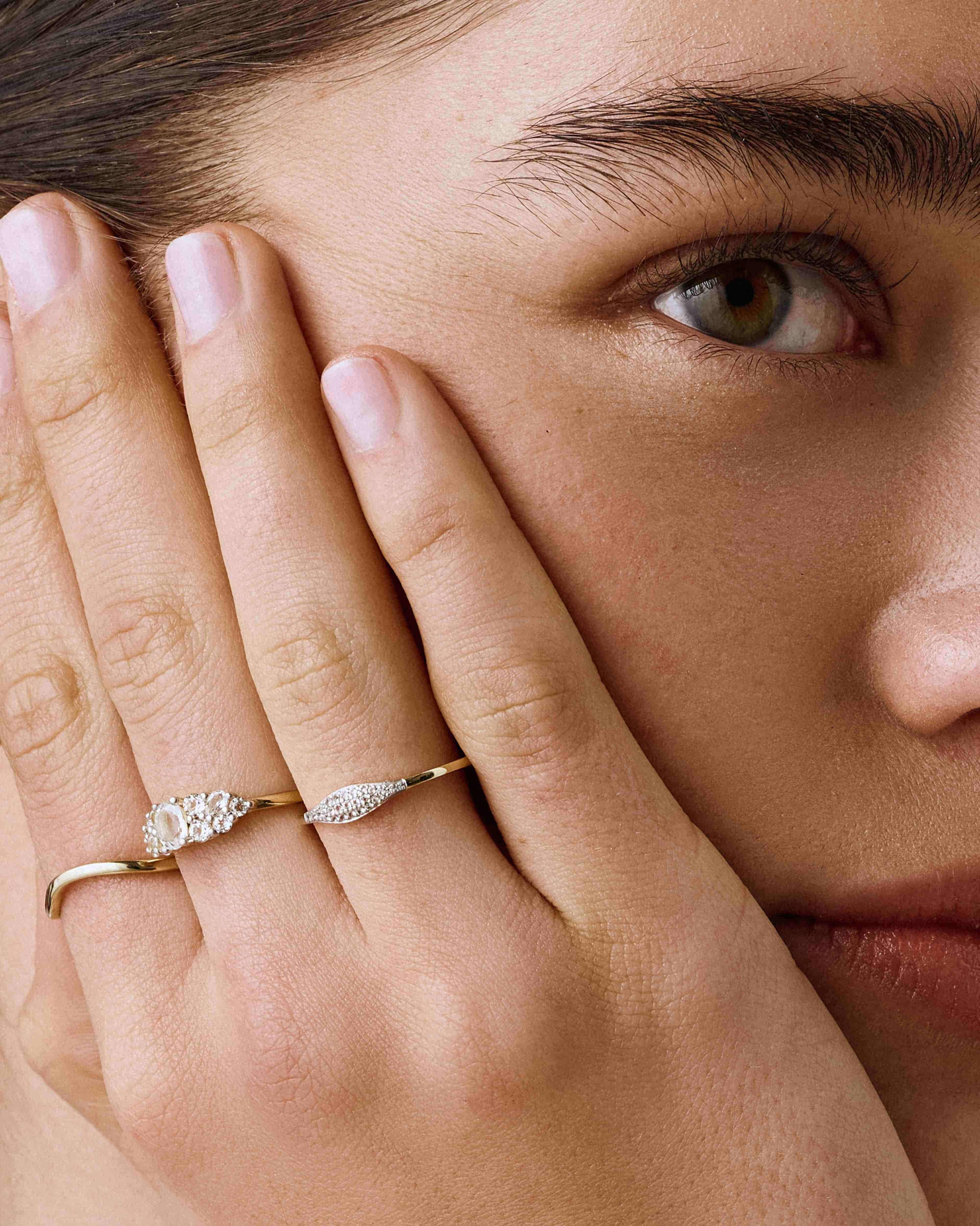 Close-up of a woman's hand with two gold rings on a neutral background